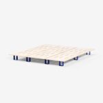 Ein minimalistisches Bettgestell aus hellem Holz mit horizontalen Latten und kurzen, blauen, rechteckigen Beinen, das auf einem schlichten weißen Hintergrund abgebildet ist.