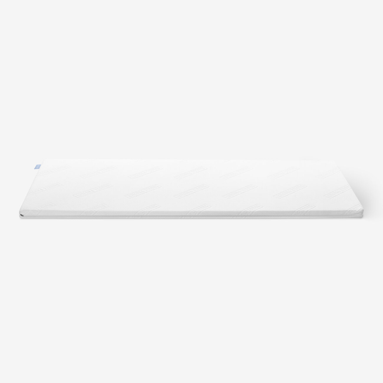 Eine weiße, rechteckige Matratzenauflage mit einem minimalen Strukturmuster auf einem schlichten, hellen Hintergrund.